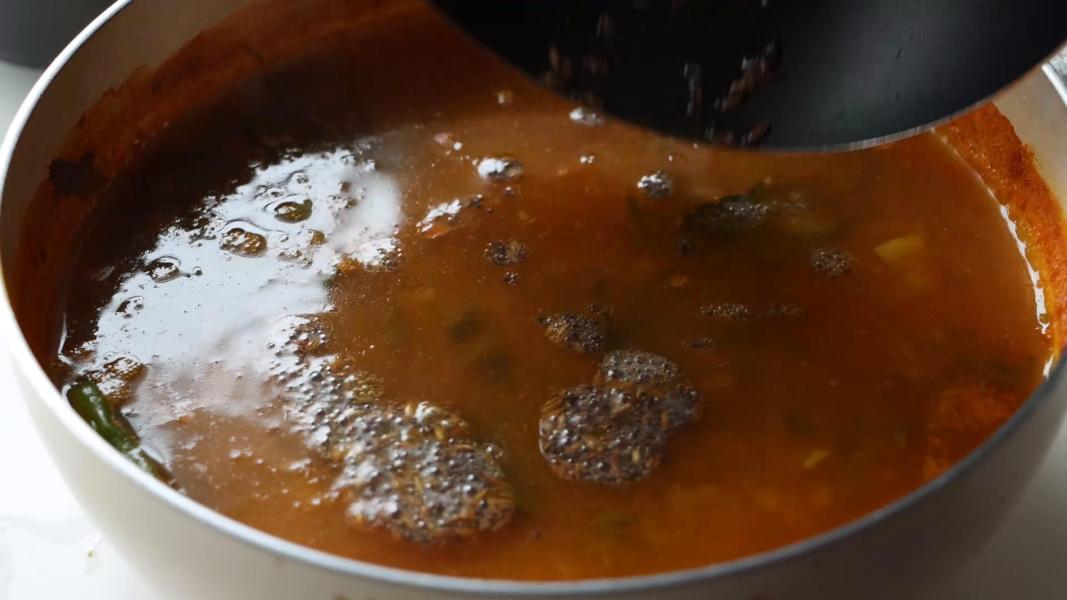 pouring the tempered mustard seeds and cumin seeds into the green mango rasam