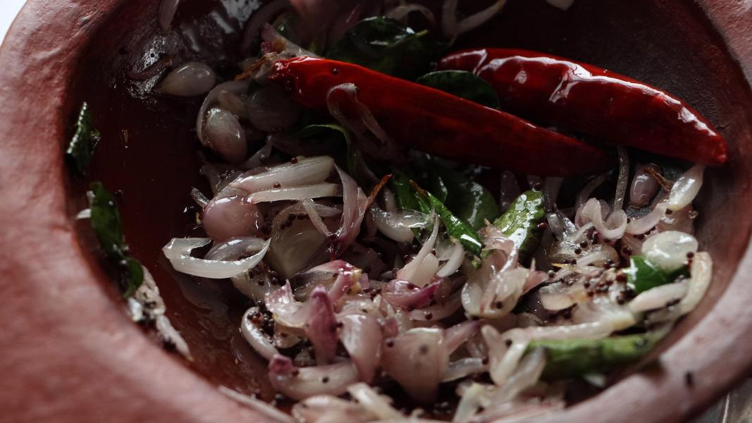 shallots are sauteed along with red chillies and curry leaves in a small clay pan.