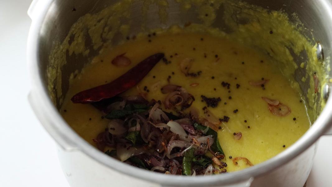 Sauteed shallots are added to the prepared dal-coconut mixture in a pressure cooker.