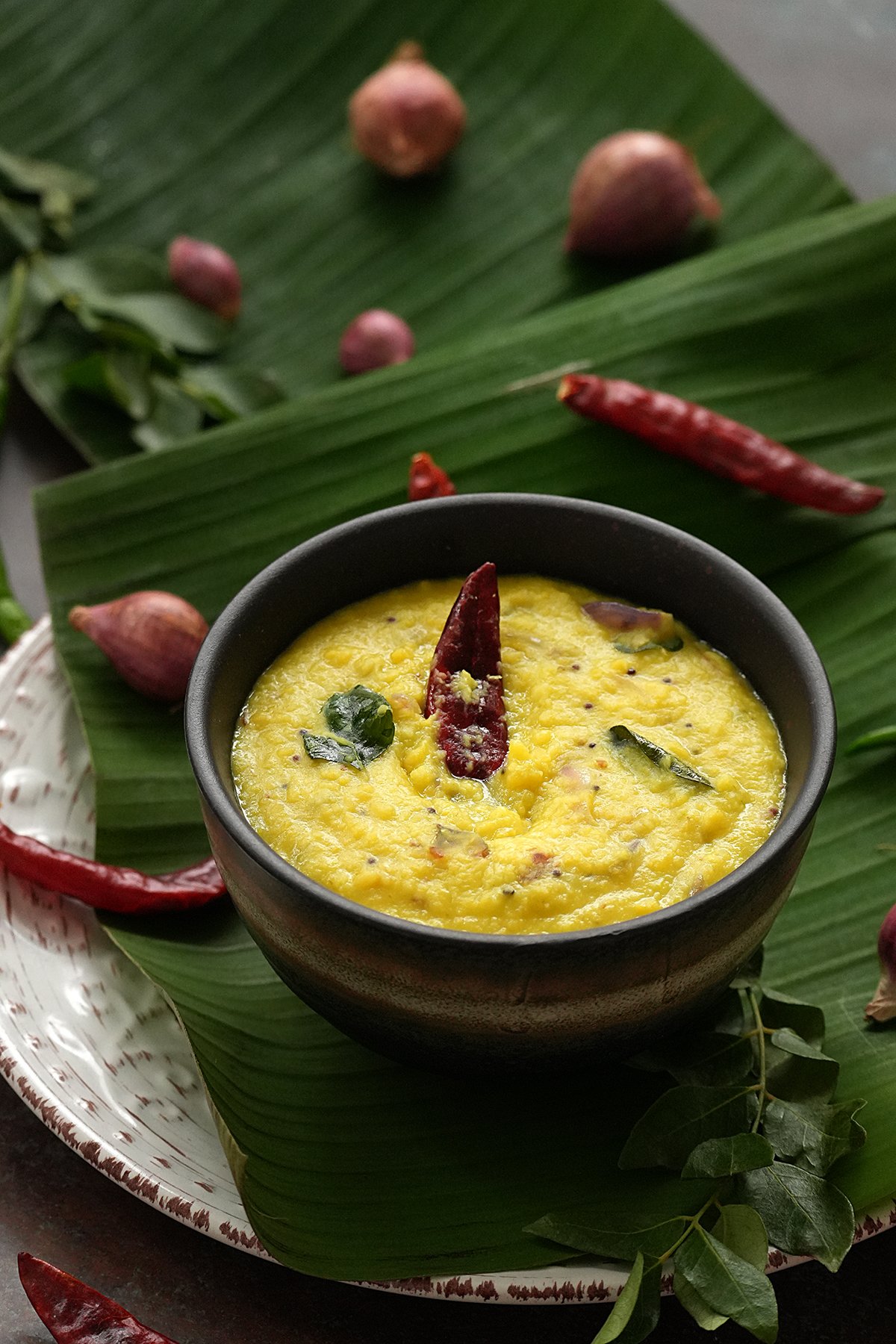 kerala style parippu curry in a stone bowl topped with a red chilli and curry leaves and placed on banana leaf