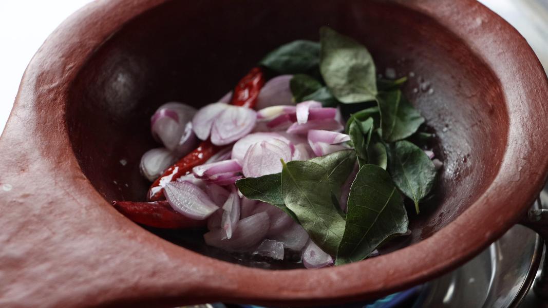 Shallots, red chillies, curry leaves added to a tempering in a small clay pan.