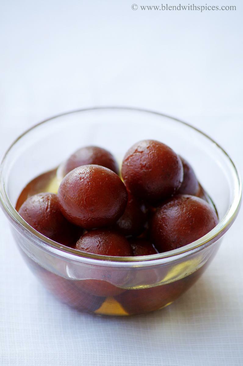 Traditional Indian gulab jamuns in sugar syrup served in a transparent glass bowl.