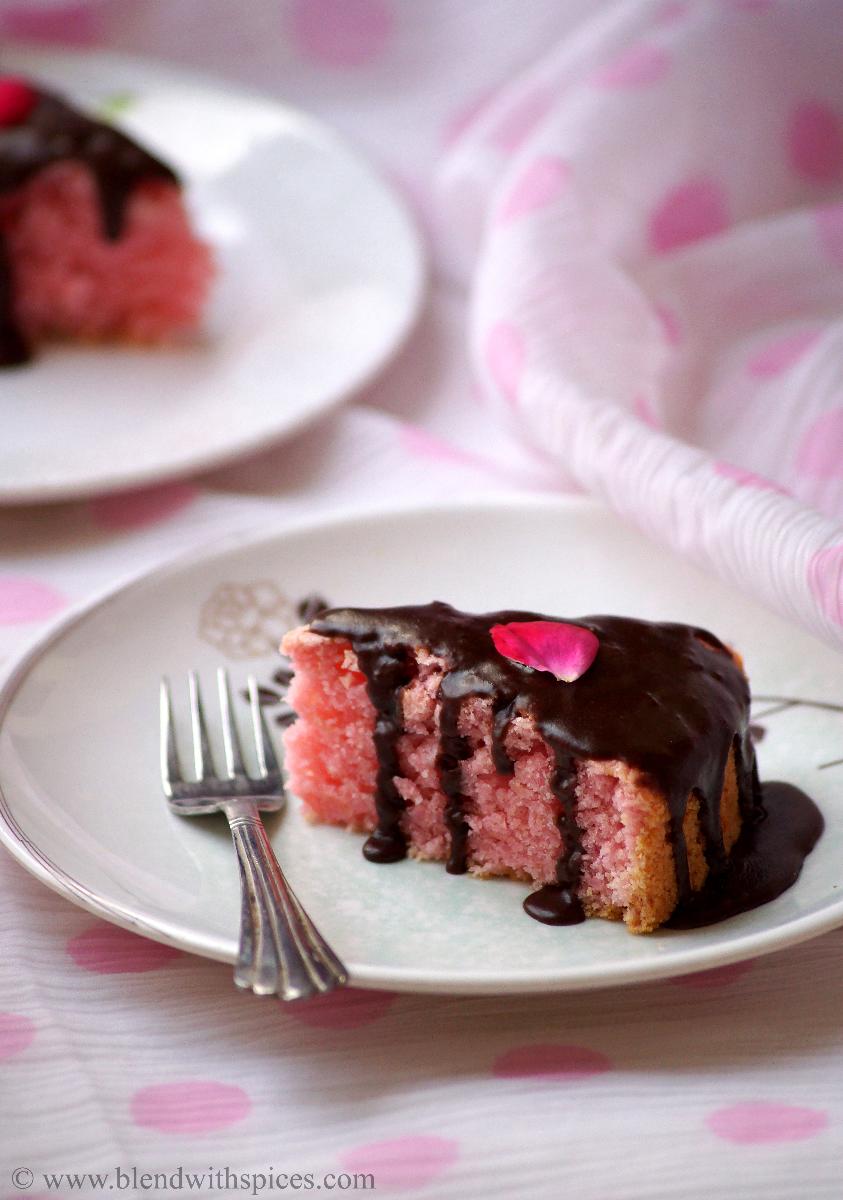 pink color eggless cake topped with chocolate sauce and rose petal and served in a plate with a fork.