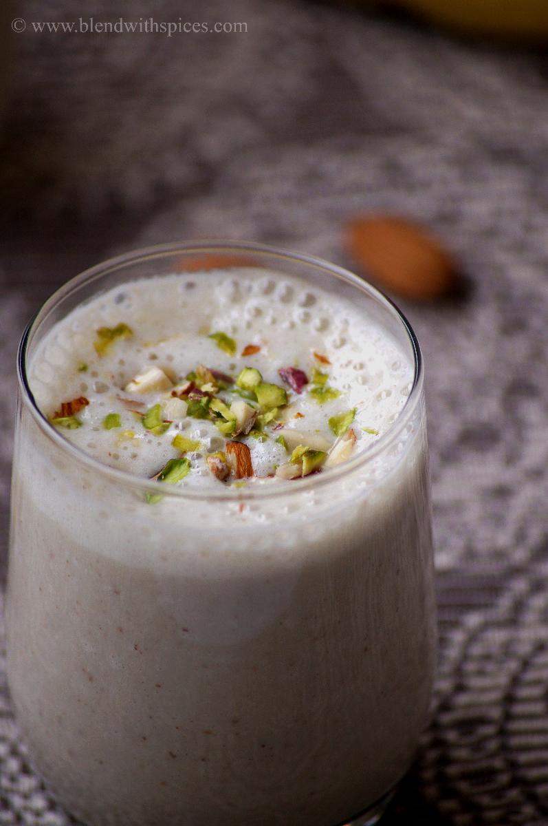 banana milkshake served in a glass garnished with chopped almonds and pistachios
