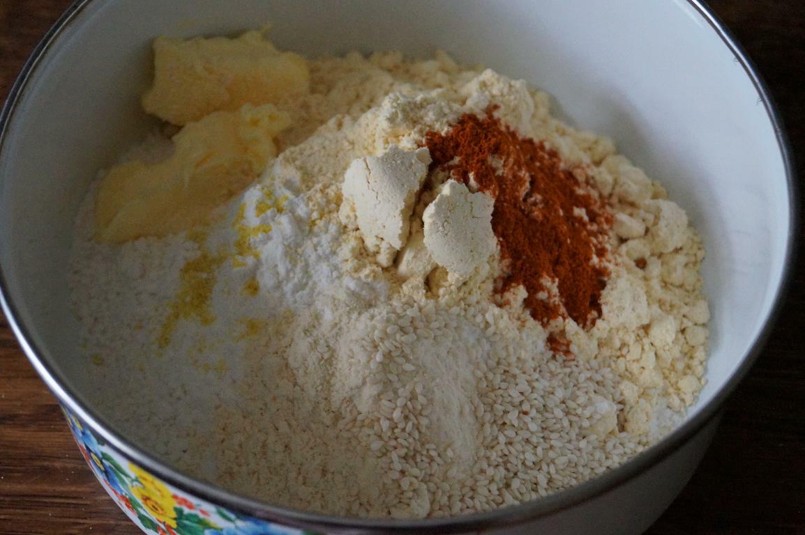 Ingredients for ribbon pakoda including rice flour, besan, roasted gram flour, butter, sesame seeds, and spices in a mixing bowl to make dough.
