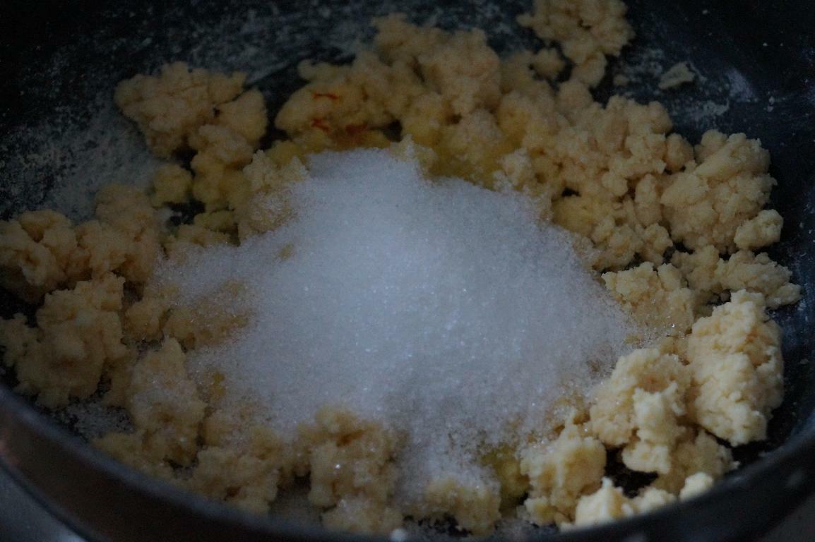 Adding sugar, cardamom and saffron-infused milk to cooked khoya mixture for tutti frutti kesar burfi.