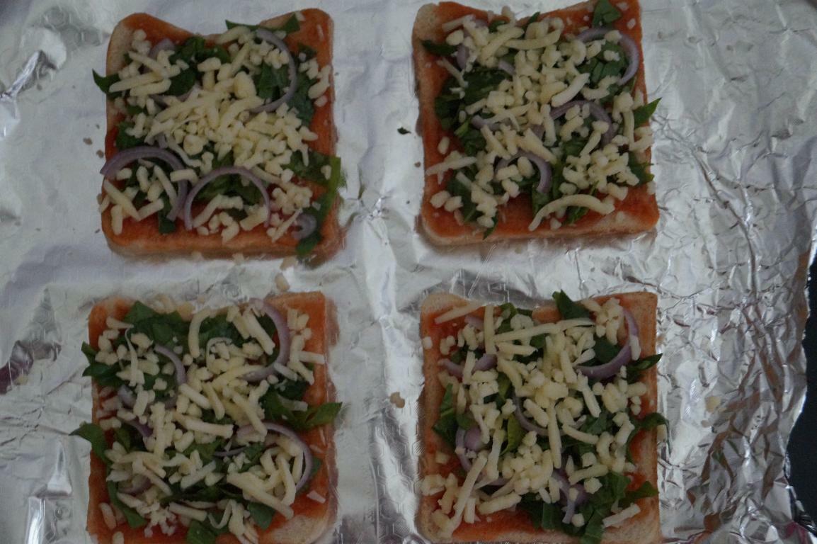 Pizza sauce, spinach, onion, cheese and seasonings are added to the bread slices and arranged on a lined baking tray to make homemade spinach bread pizza
