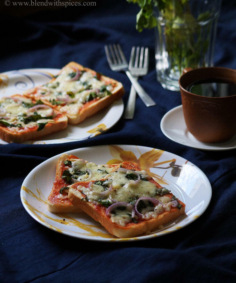 Homemade spinach bread pizzas are served on plates along with a cup of tea.