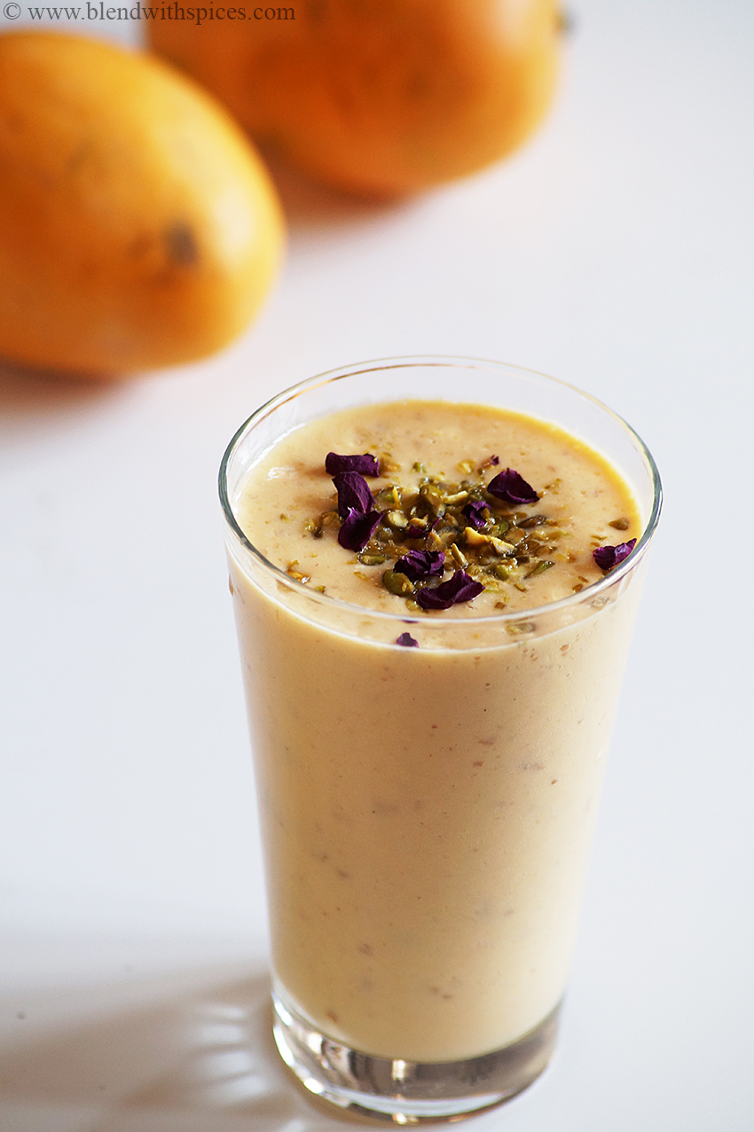 A glass of mango gulkand lassi garnished with chopped pistachios and rose petals