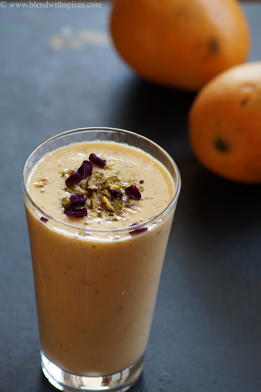 A glass of chilled mango gulkand lassi topped with pistachios and dried rose petals