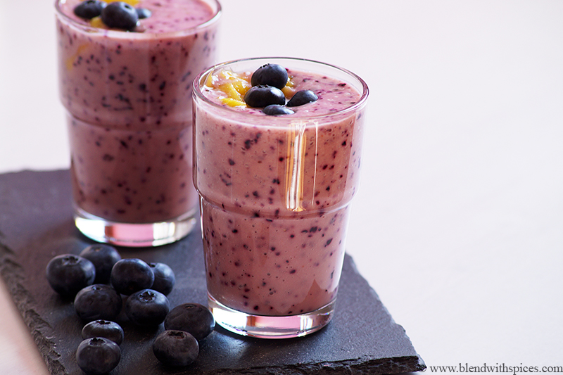 two glasses contained with blueberry mango smoothie and decorated with blueberries