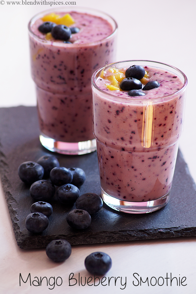two glasses of smoothie garnished with mango chunks and blueberries