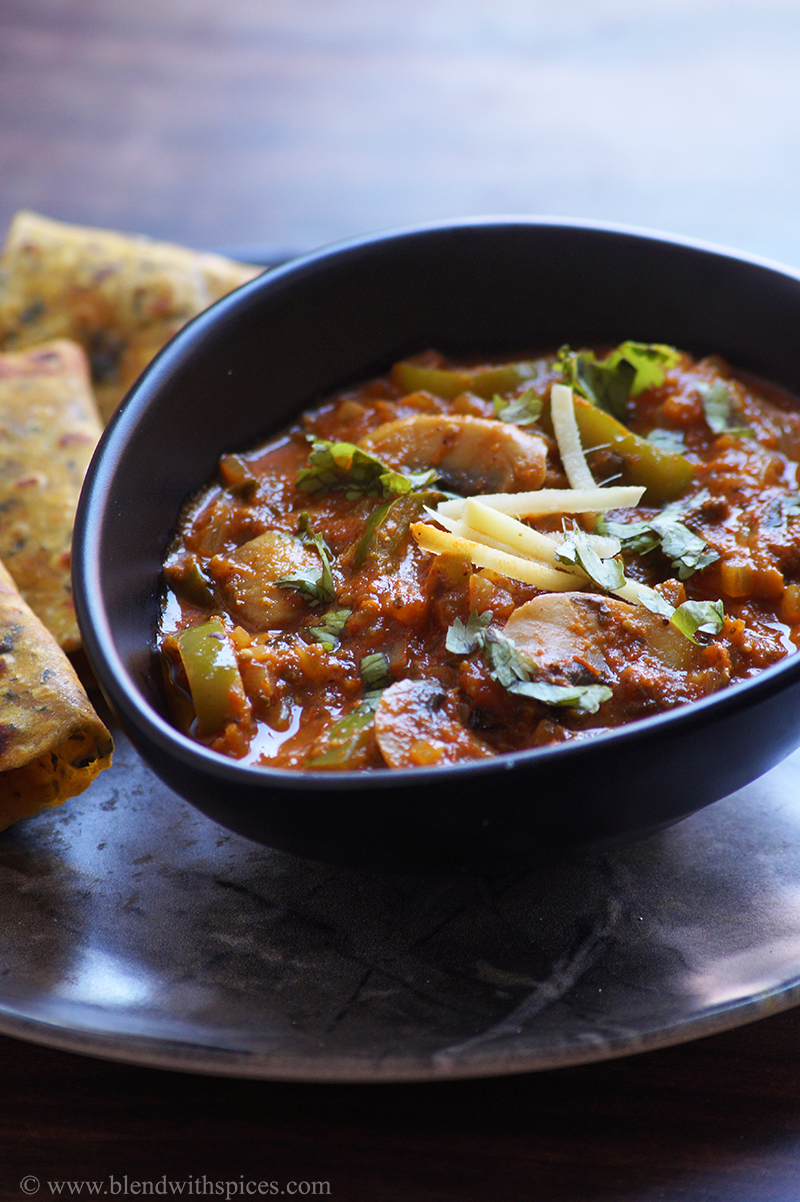 kadai mushroom curry served in a black bowl along with parathas