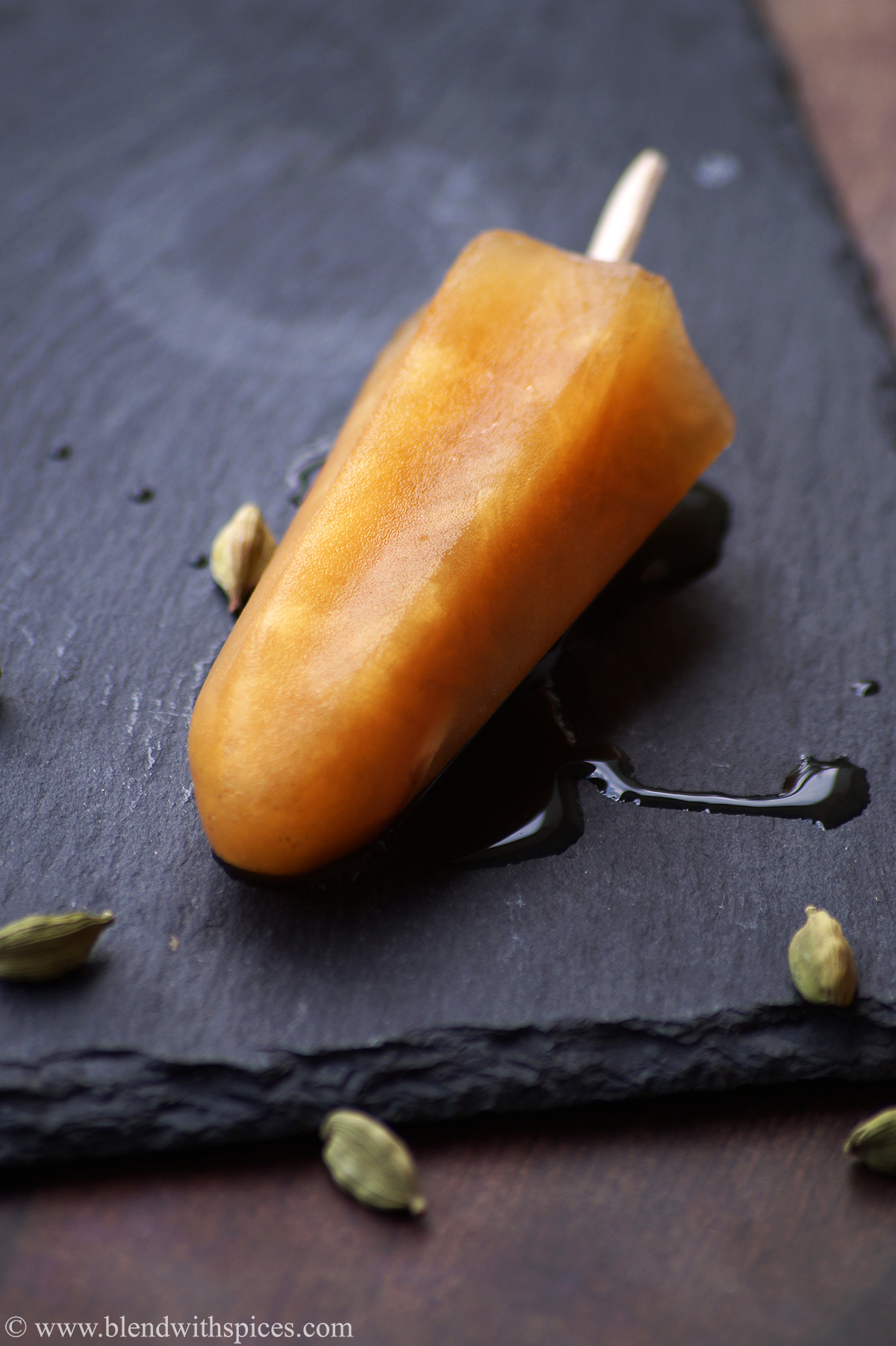 yellow colored jaggery ice popsicle decorated with cardamom pods