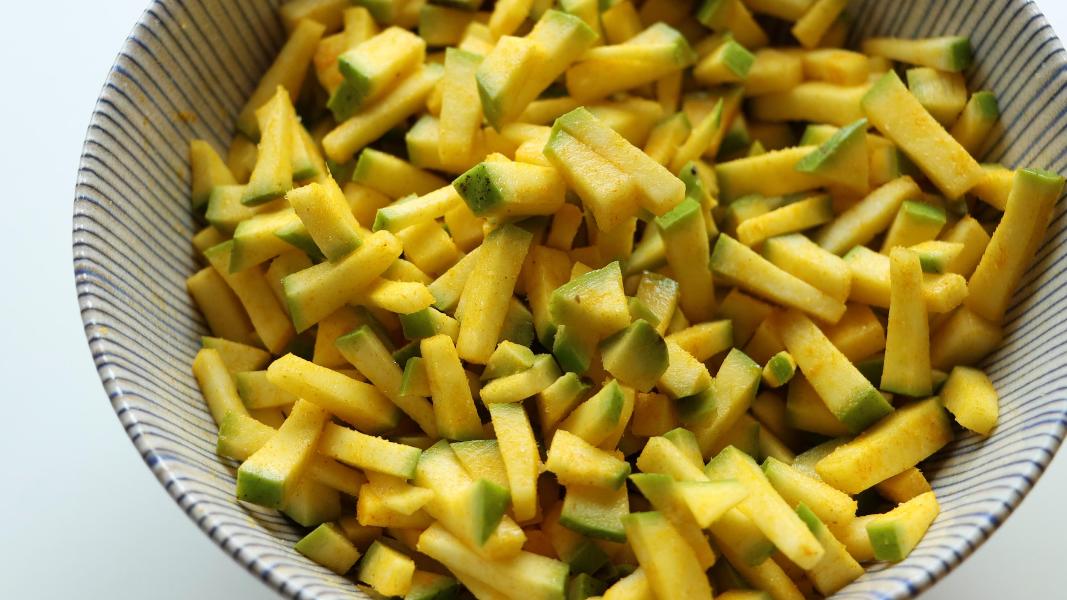Chopped raw mangoes are marinated with salt and turmeric powder and resting in a bowl on a countertop 