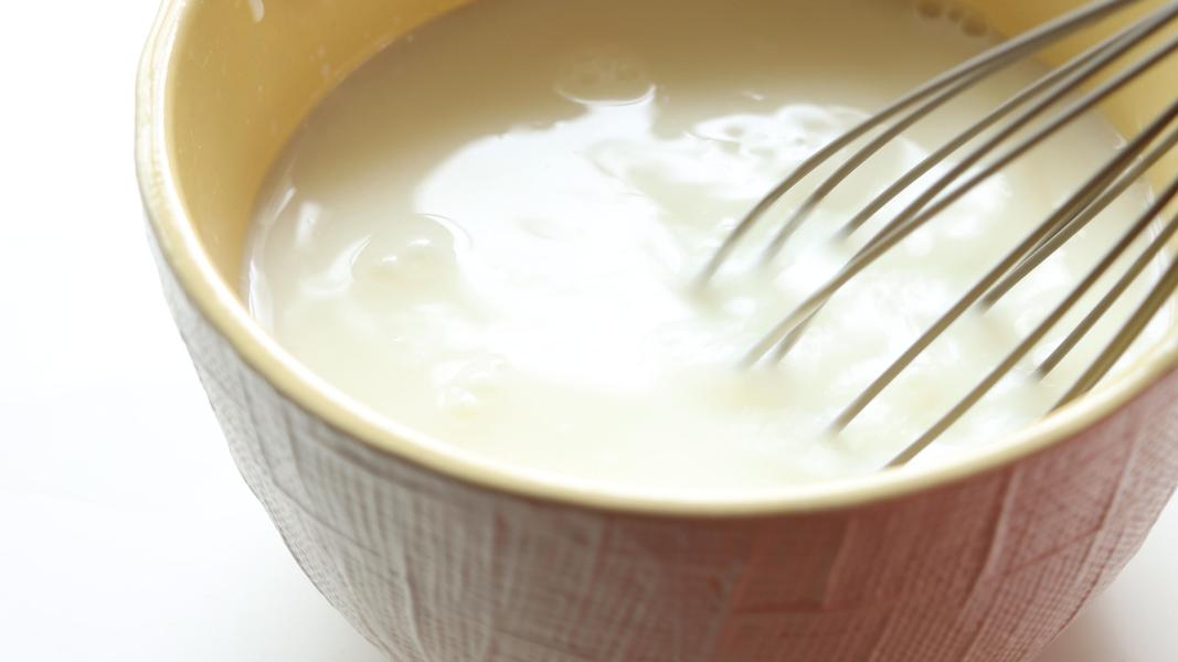 whisking yogurt with water in a yellow mixing bowl