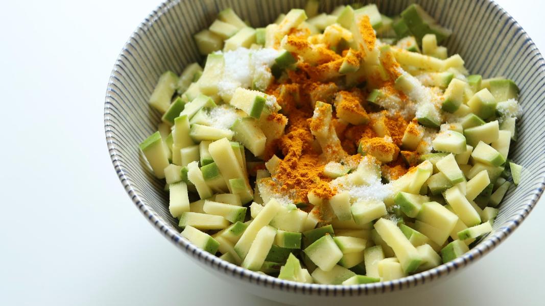 Chopped green mangoes sprinkled with salt and turmeric powder in a mixing bowl