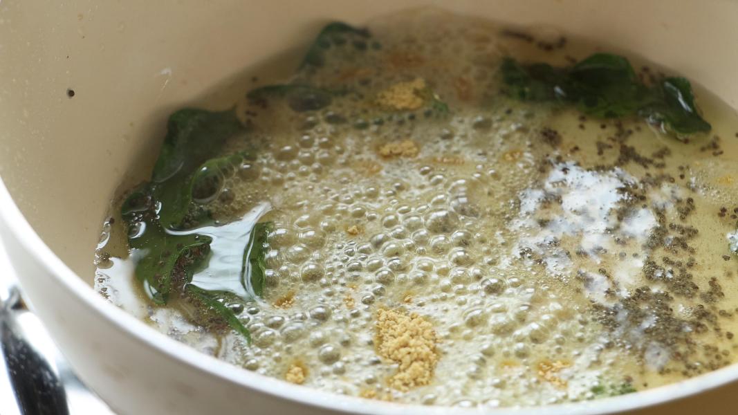 Tempered mustard seeds, curry leaves with sesame oil in a frying pan