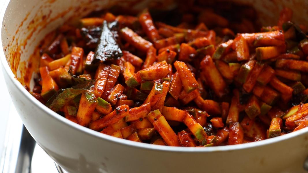 Marinated green mango pieces are coated with tempered chili powder mixture in a frying pan