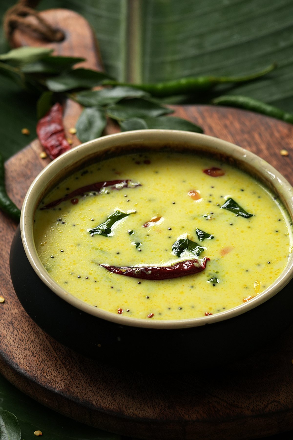 a bowl of moru curry topped with curry leaves and red chilies