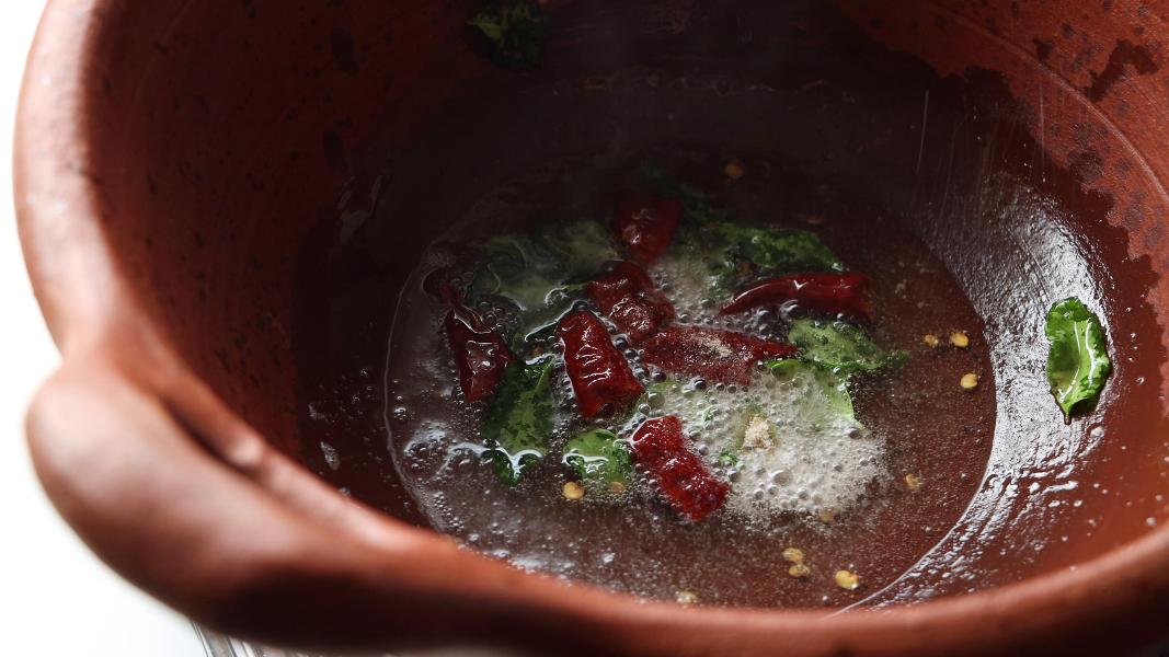 Tempering mustard seeds, dried red chilies, curry leaves and hing in a clay pot