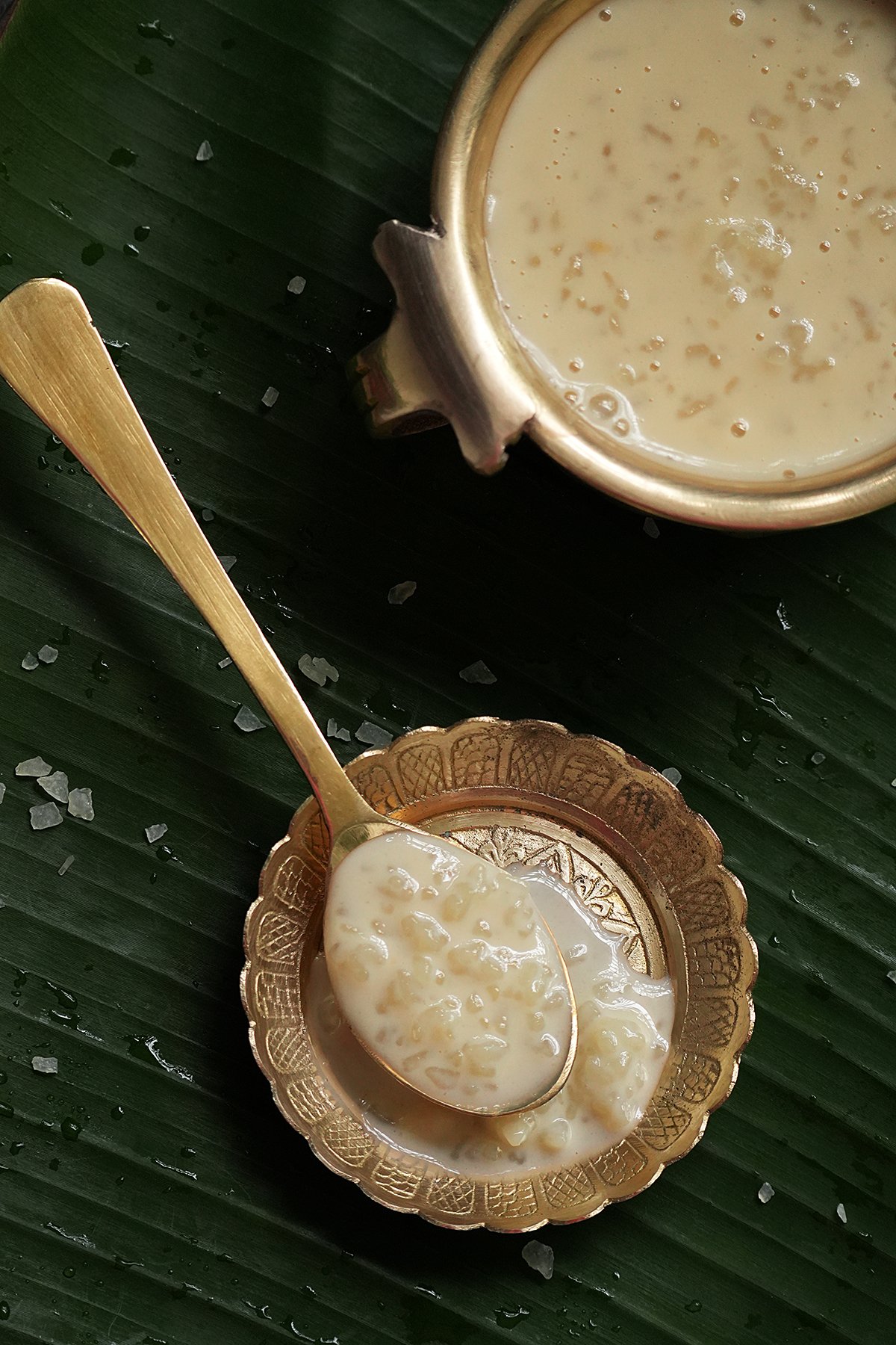A spoonful of kerala ada pradhaman on a small brass plate, with a side of a bowlful of ada pradhaman on a banana leaf