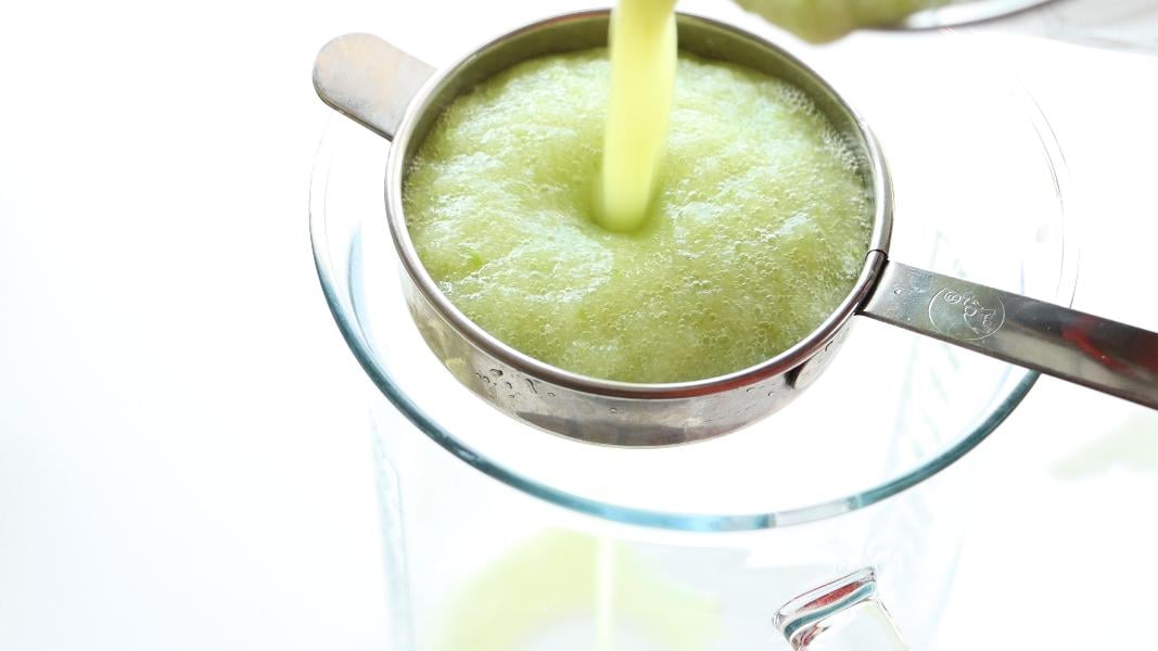 Straining the blended green apple juice through a steel strainer to get a clear green apple juice. 