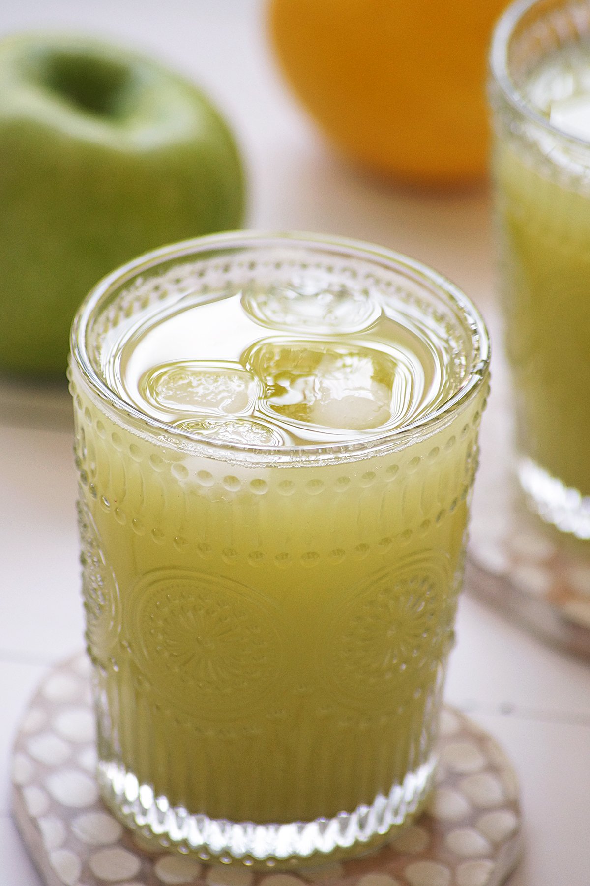 Green apple juice served in embossed clear glasses along with few ice cubes