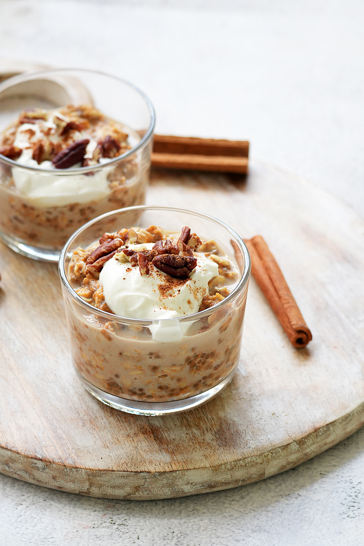Pumpkin pie overnight oats served in small glass cups and placed on a wooden board