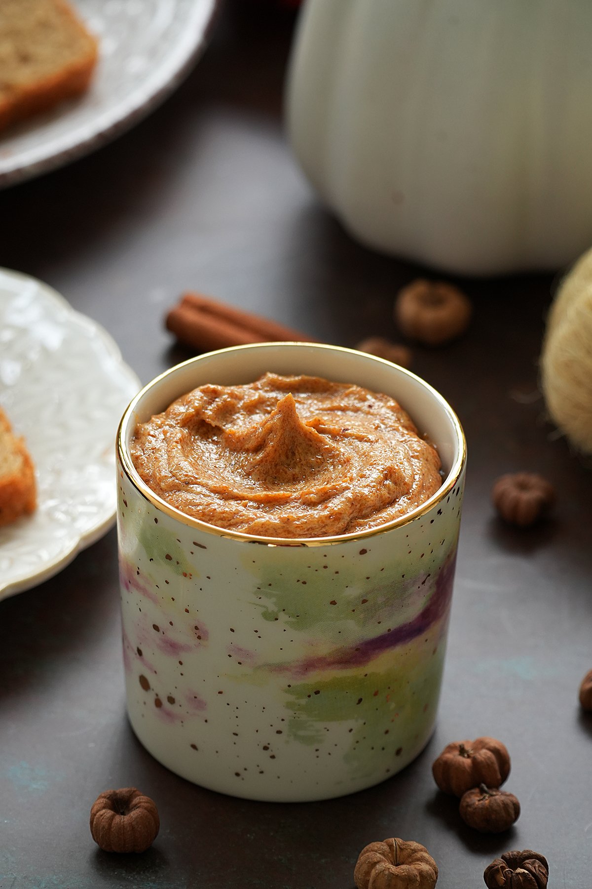 A cup of pumpkin pie spice butter, surrounded by cinnamon sticks and fall decorations.