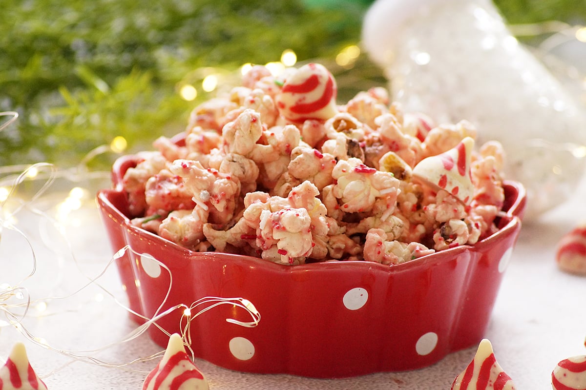 Candy cane kiss popcorn served in a red bowl, made with popcorn coated in melted peppermint kisses and festive sprinkles.