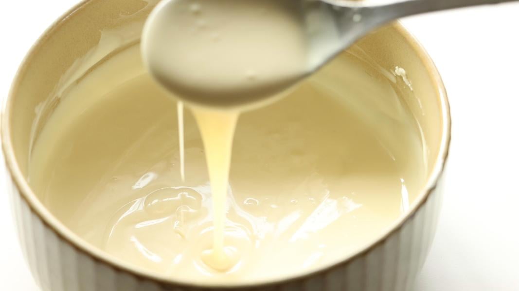 Melted white chocolate pouring from a spoon into the ceramic bowl.