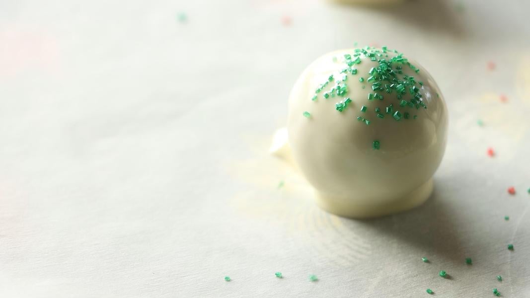 Chocolate covered gingerbread truffle placed on a lined tray, green sparkling sugar added on top. 