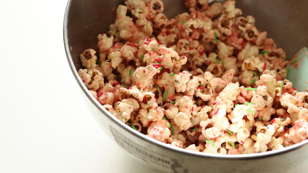 Popcorn mixed with melted peppermint kisses and sprinkles in a large mixing bowl.