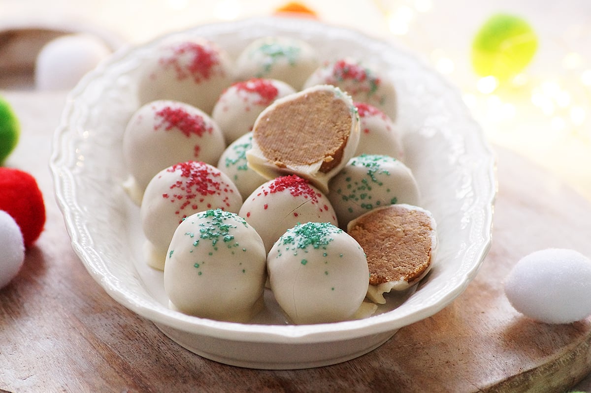 Gingerbread truffles covered with white chocolate and decorated with Christmas sparkling sugar served on a white decorative tray.