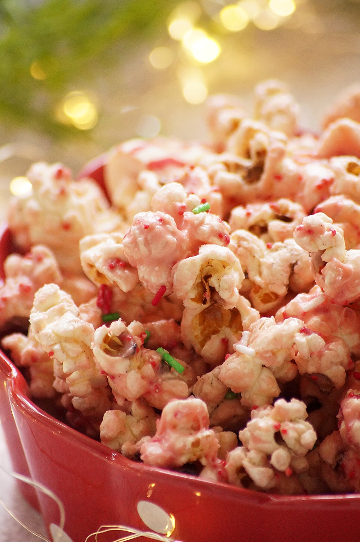 A close-up shot of Candy cane kiss popcorn served in a red bowl, made with popcorn coated in melted peppermint kisses and festive sprinkles.