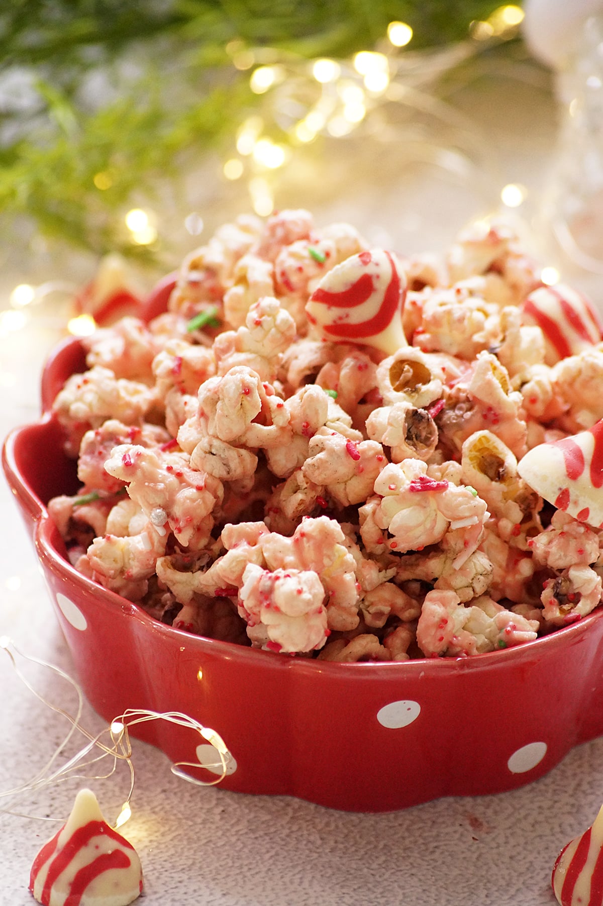Candy cane kiss popcorn served in a red bowl, made with popcorn coated in melted peppermint kisses and festive sprinkles.