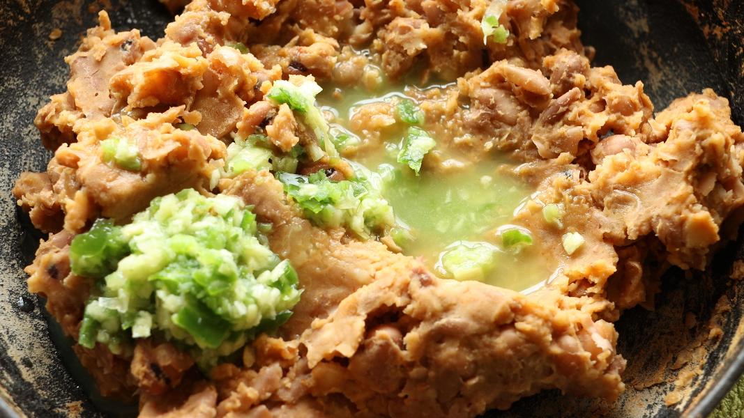 Mashed fava beans topped with garlic jalapeno sauce before mixing for foul medames.