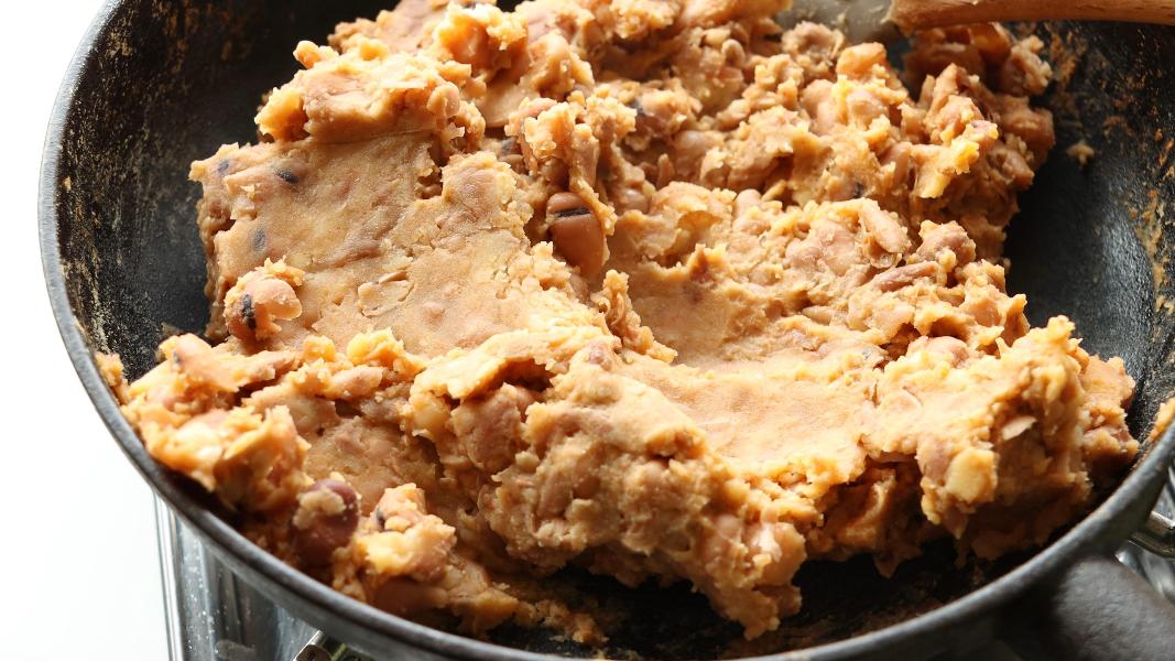 Partially mashed fava beans in a pan showing thick and creamy texture for ful medames preparation.
