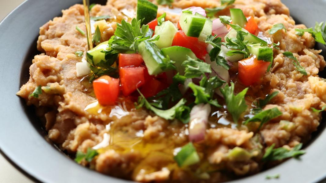 Traditional Egyptian ful medames topped with olive oil, cucumber, onion, tomato and parsley and ready to serve with bread.