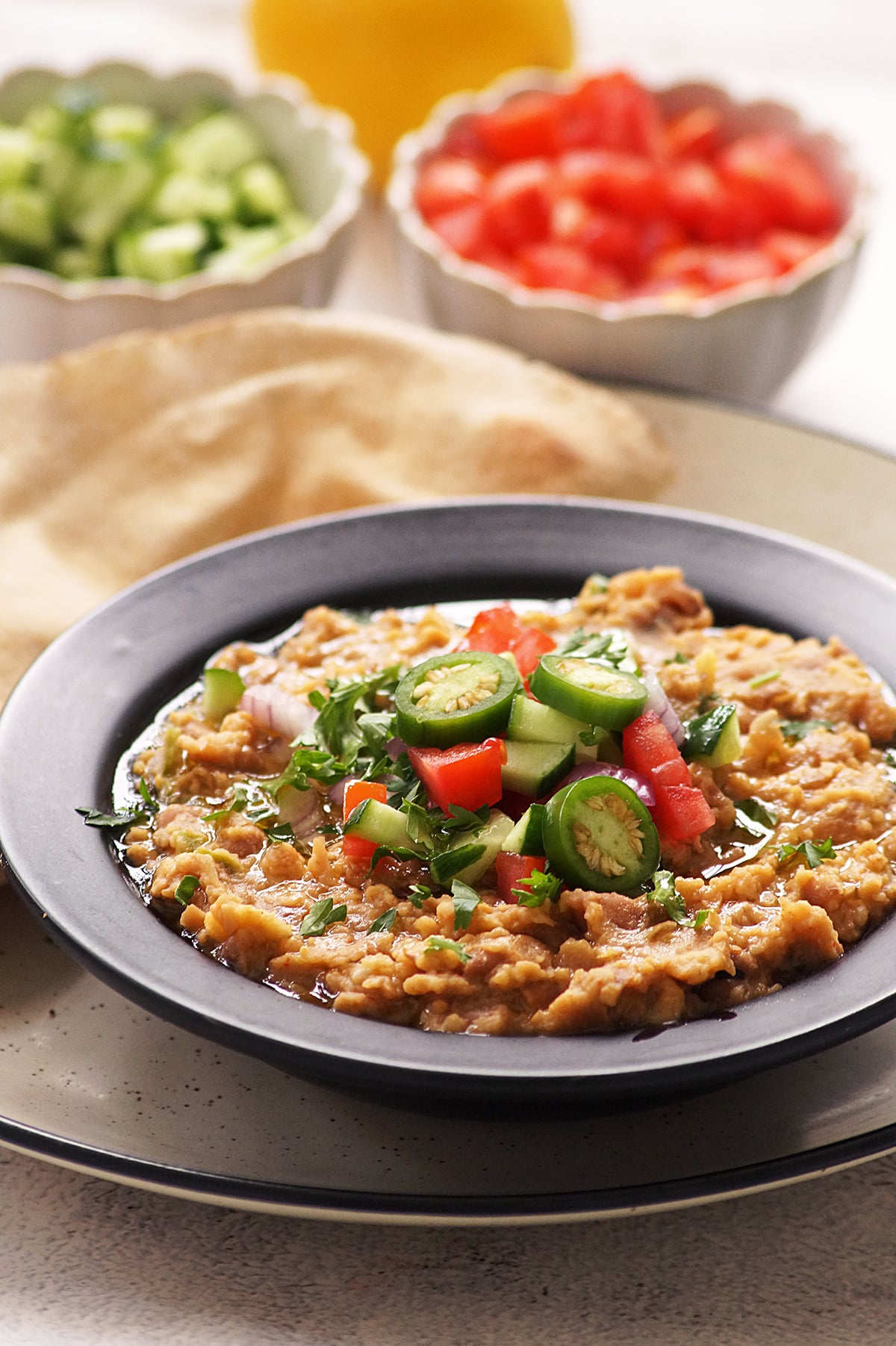 A close-up image of traditional Egyptian Foul Mudammas or Ful Medames topped with olive oil, fresh salad and jalapeno. Served with pita bread.