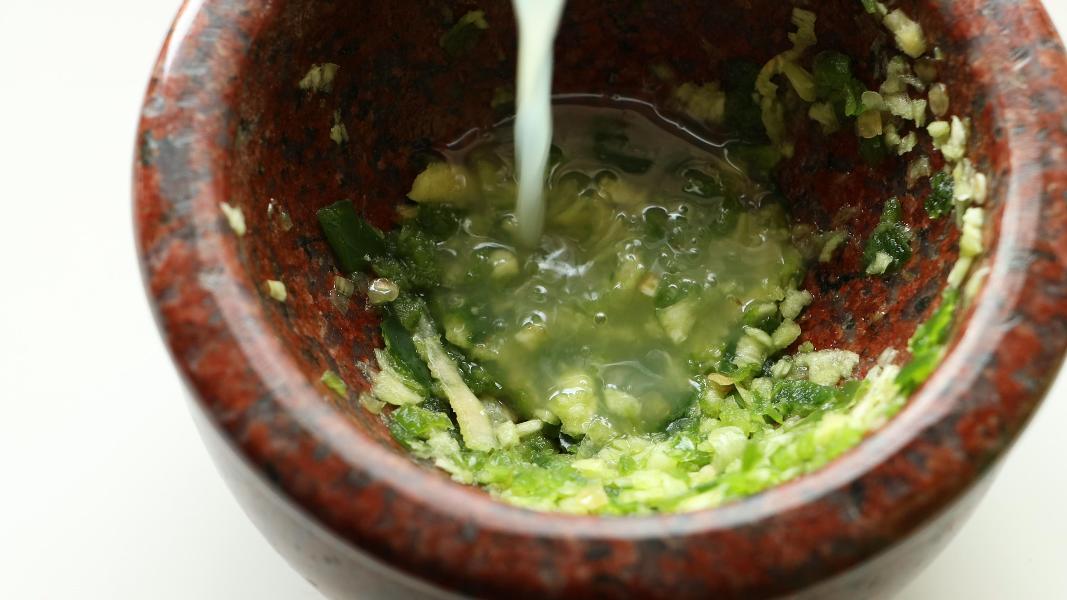 Adding salt and lemon juice to the crushed garlic and jalapeno mixture for preparing ful mudammas sauce