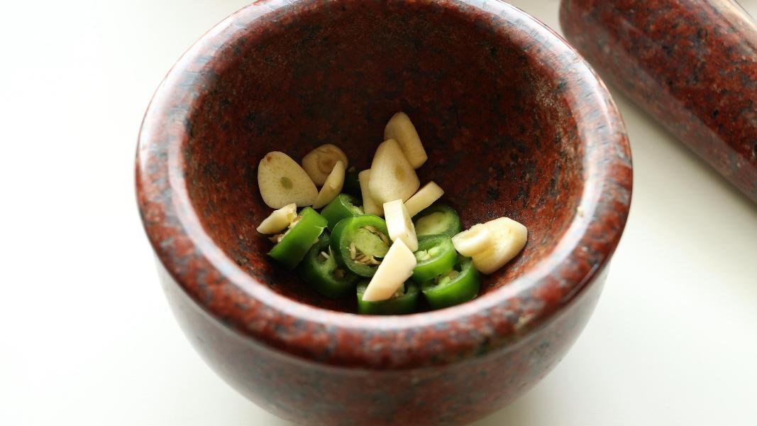 Sliced garlic cloves and sliced jalapeños in a mortar ready to be crushed for ful medames sauce.