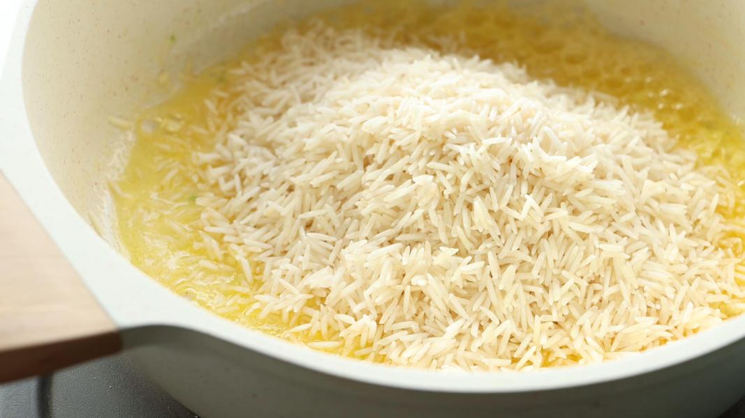 Adding rinsed long-grain rice to the garlic butter mixture to make parmesan rice.