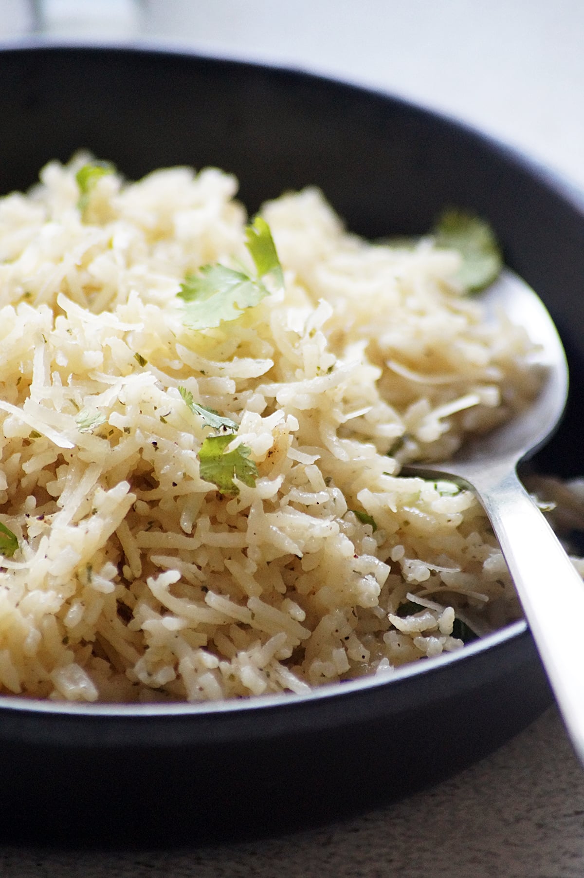 A close-up capture of Garlic Parmesan rice with fluffy long-grain rice, grated Parmesan cheese, and fresh parsley served in a black bowl.